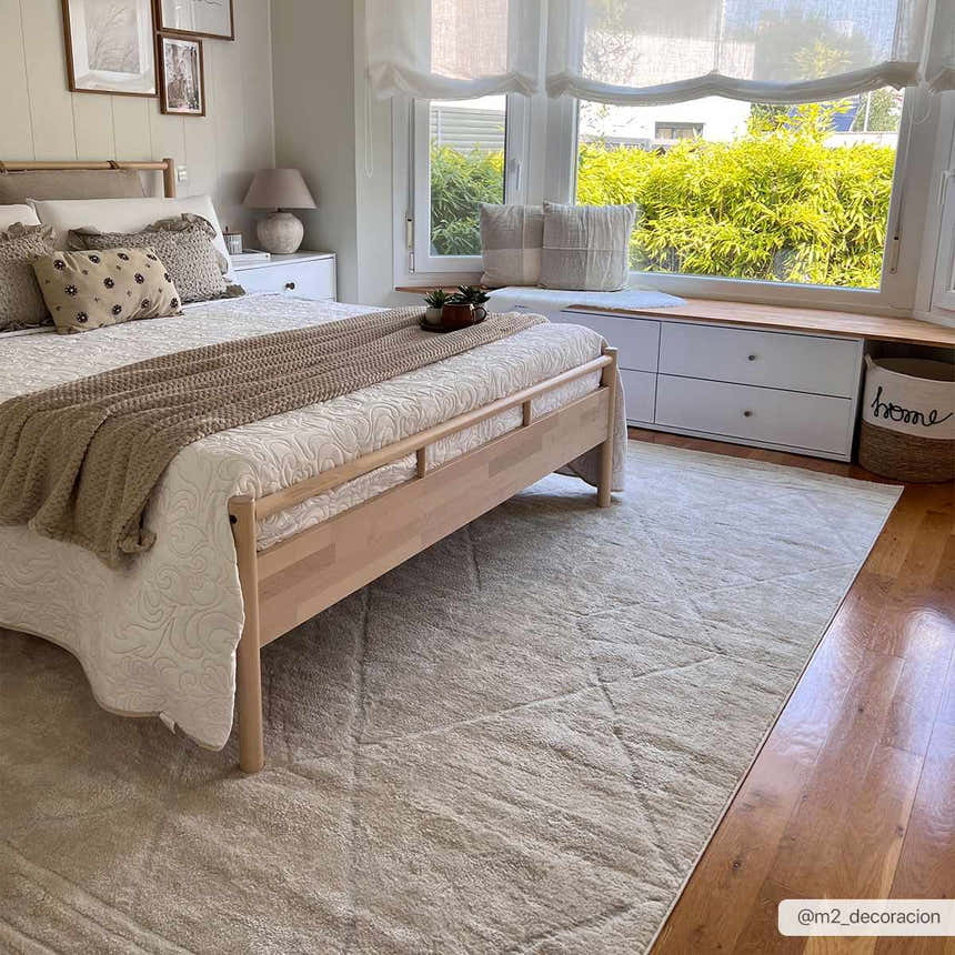 Bedroom scene with a Keanu Ivory area rug, wood bed frame, and window seat. Neutral beige and off-white tones. Roomscene-Rectangle