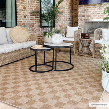 Outdoor patio scene with a Kuval Checkered Brown Rug, wicker furniture, and brick fireplace. Camel and neutral tones create a cozy space. Roomscene-Rectangle