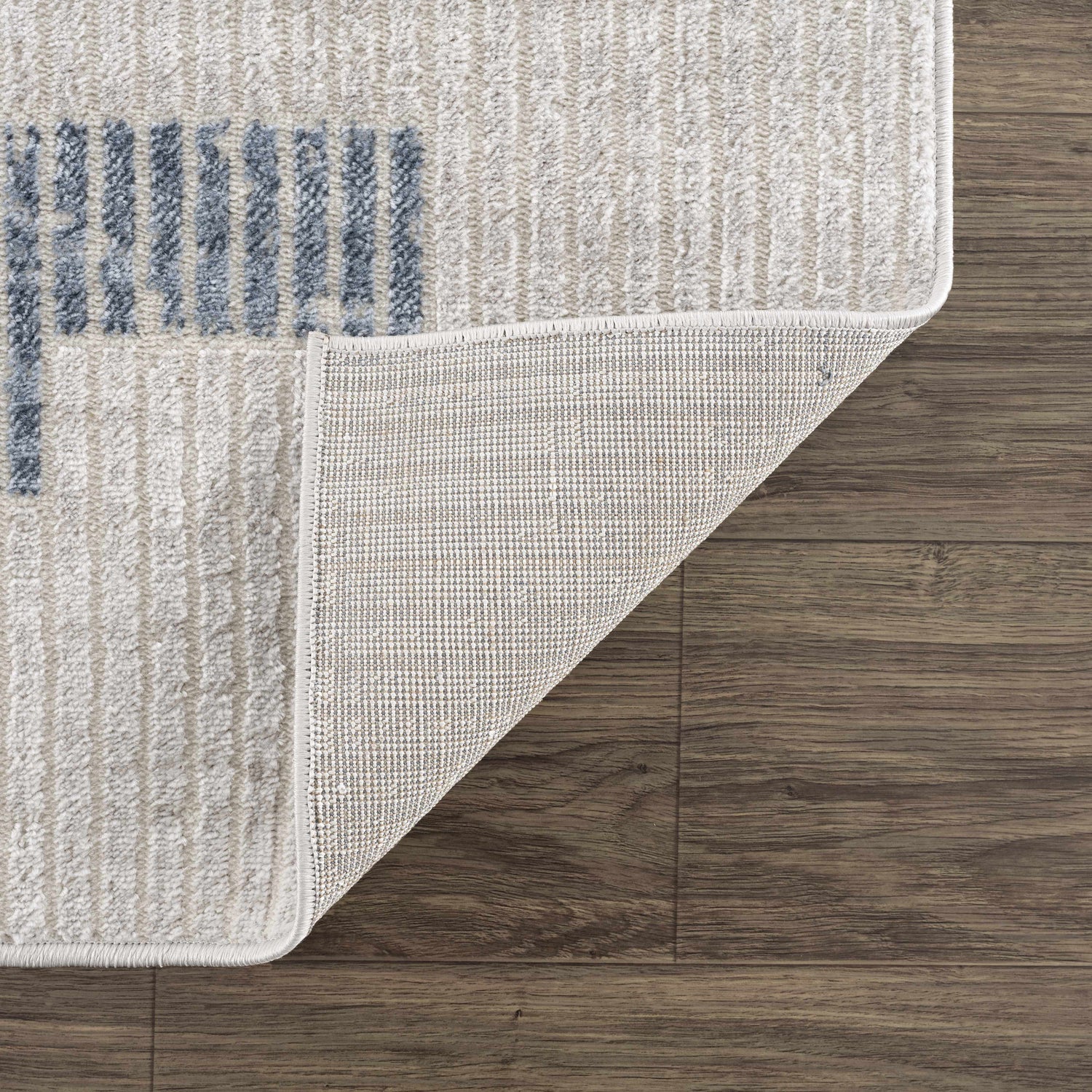 Close-up of Brisa Area Rug showing blue and gray abstract pattern and woven backing on a dark wood floor. Fold
