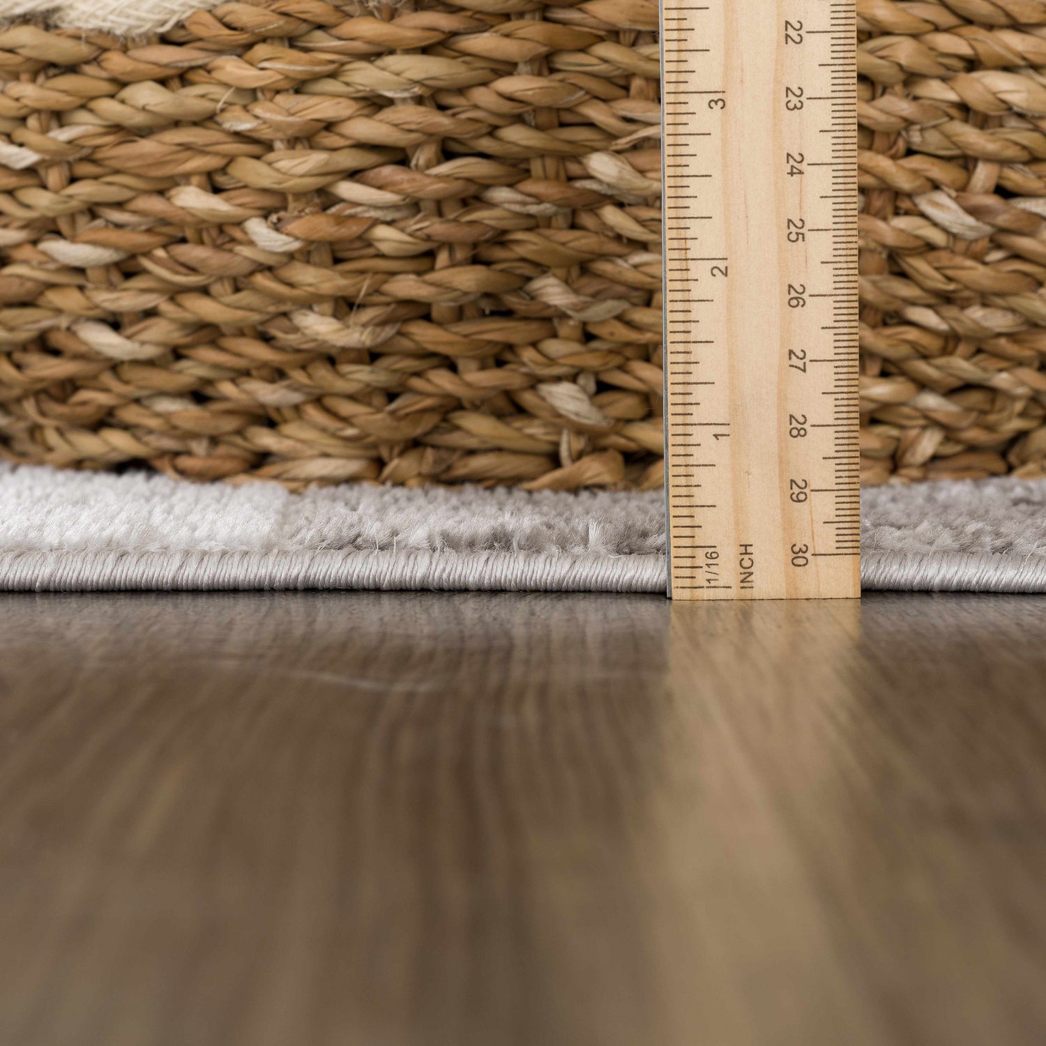 Close-up of the Brisa Area Rug showing pile height with a ruler and a woven basket on a wood floor. Pile
