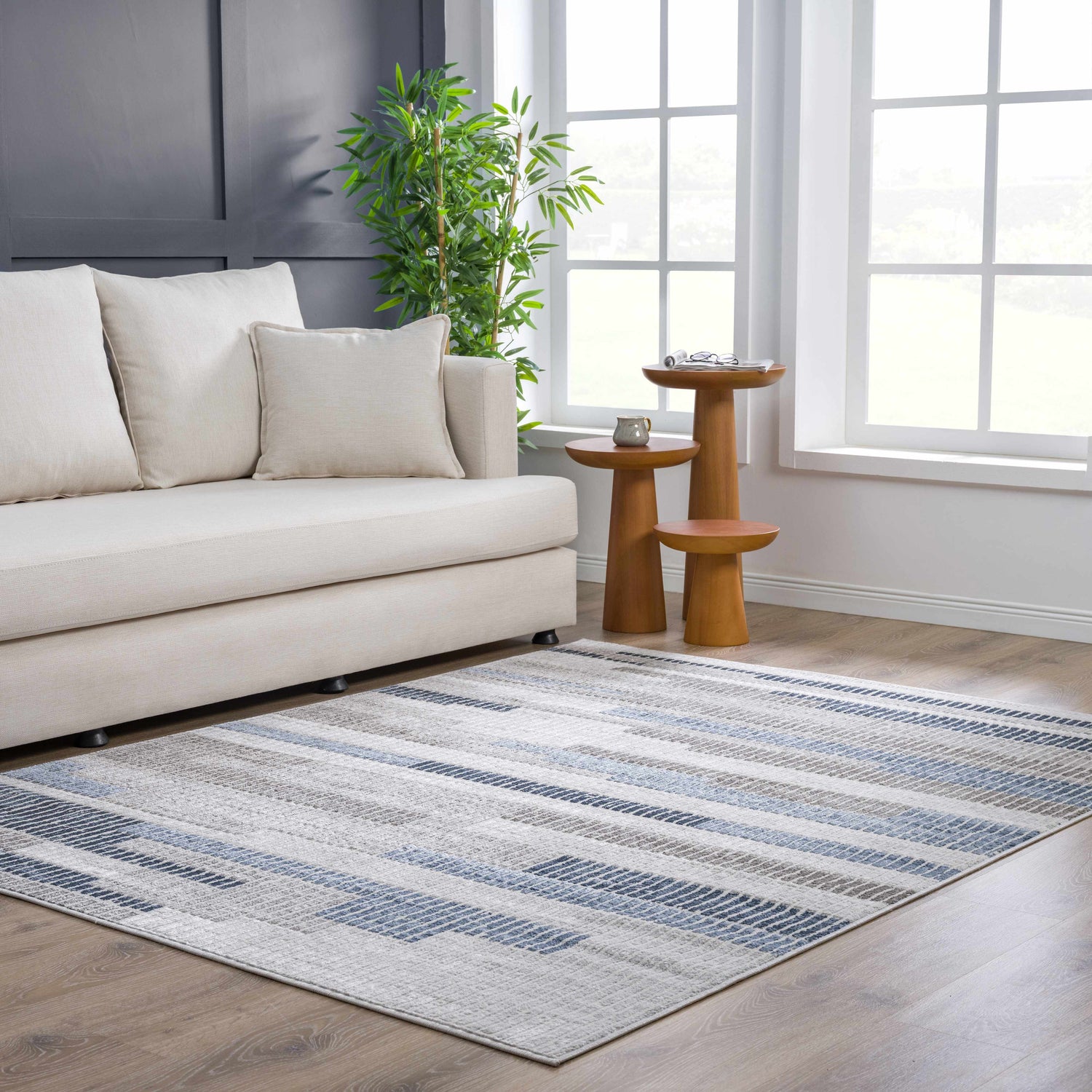 Living room scene with Brisa Area Rug in blue and gray, light sofa, wood side tables, and bright natural light. Roomscene-Rectangle