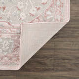 Close-up of the Zora Pink Area Rug showing its gray and pink traditional pattern and woven backing on wood floors. Fold