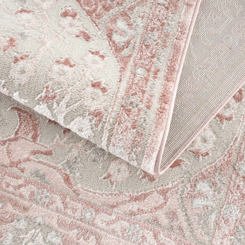 Close-up of the Zora Pink Area Rug showing its traditional vintage pattern, soft pink, and gray colors. Fold