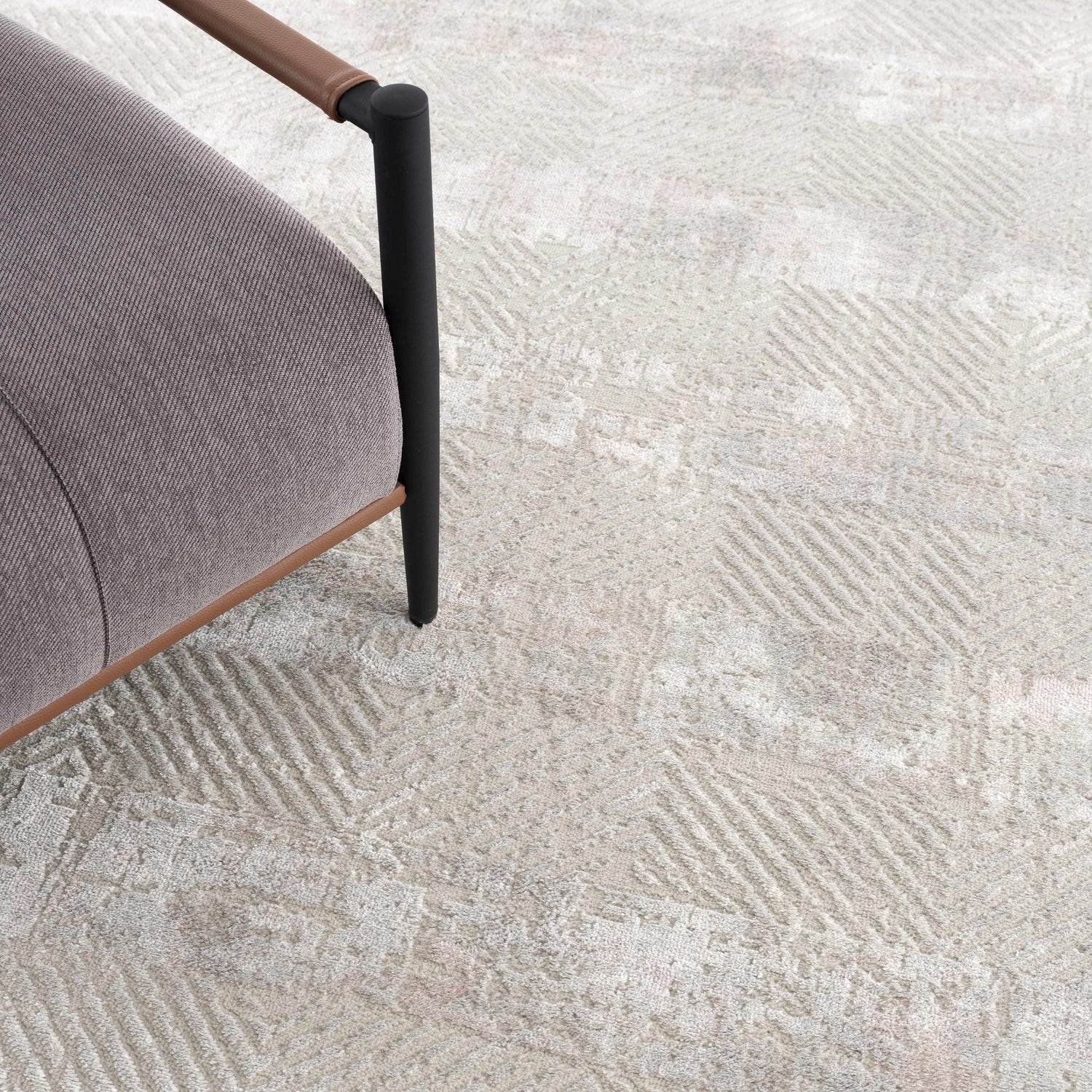 Close-up of the Bucky Area Rug showing a gray and pink geometric pattern and the texture next to a gray chair. Styleshot