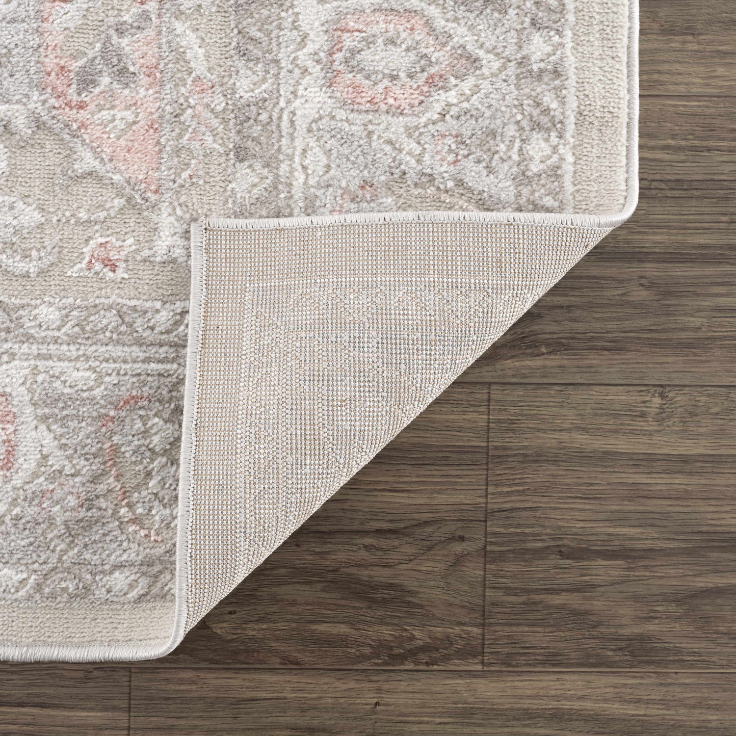 Close-up of a Damla Area Rug showing gray and pink vintage pattern, texture, and backing on wood floor. Fold