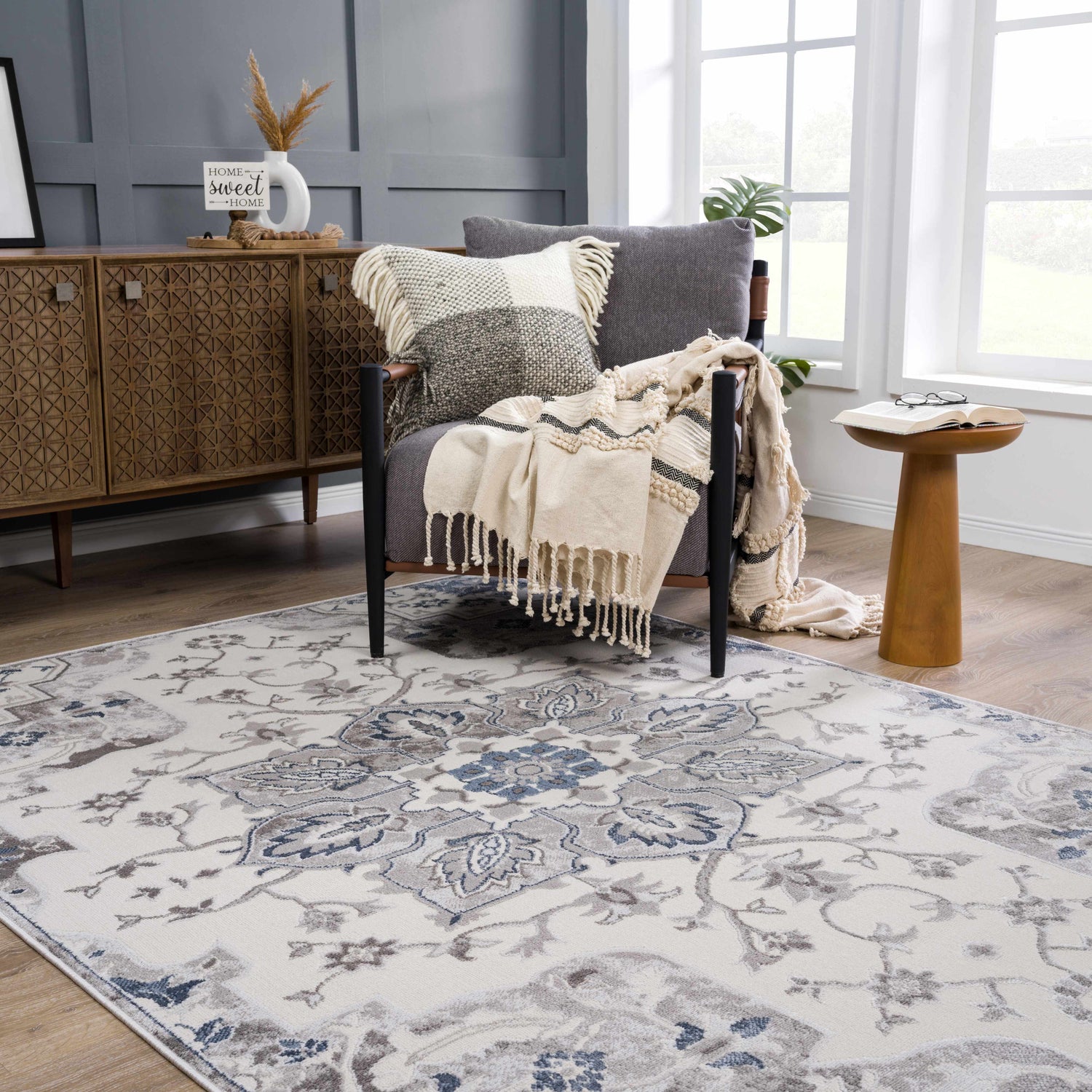 Living room scene with Calum Blue & Gray Area Rug, gray chair with throw, wooden cabinet, and natural light. Modern traditional style. Roomscene-Rectangle