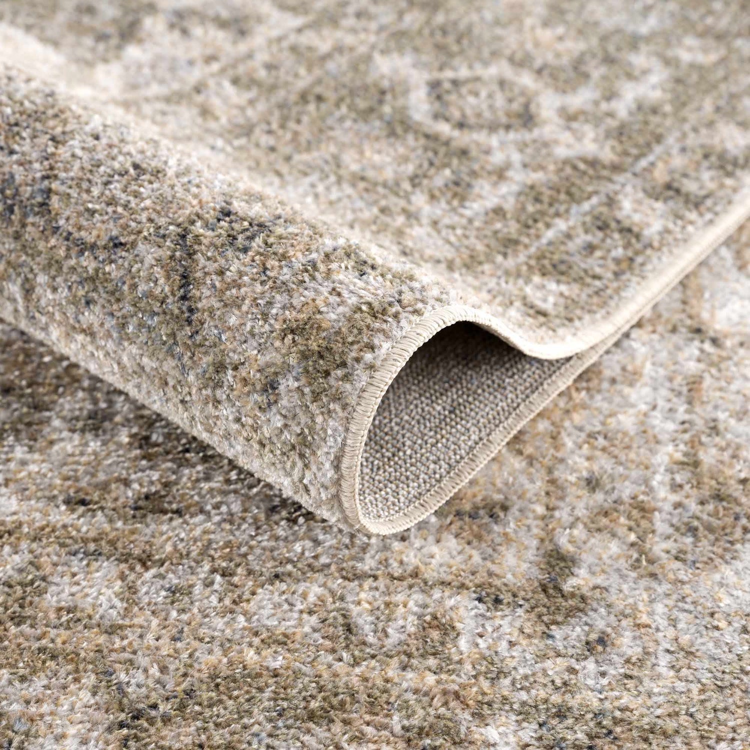 Close-up of the Gael Boutique Washable Rug showing its tan, olive, and light blue vintage pattern and soft, textured weave. Fold