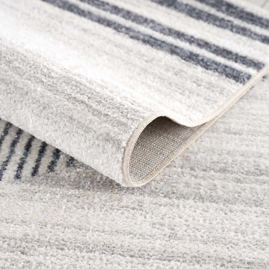 Close-up of the Thad Medium Gray Washable Area Rug showing bone and dark gray stripes and soft, textured polyester pile. Fold