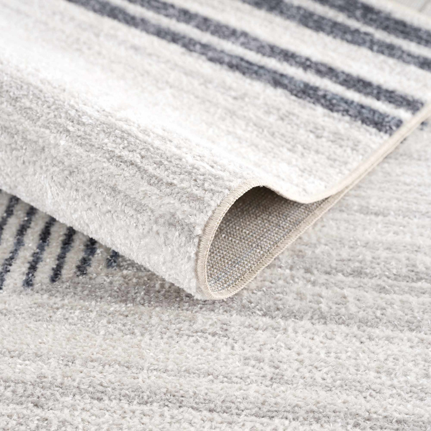 Close-up of the Thad Medium Gray Washable Area Rug showing bone and dark gray stripes and soft, textured polyester pile. Fold