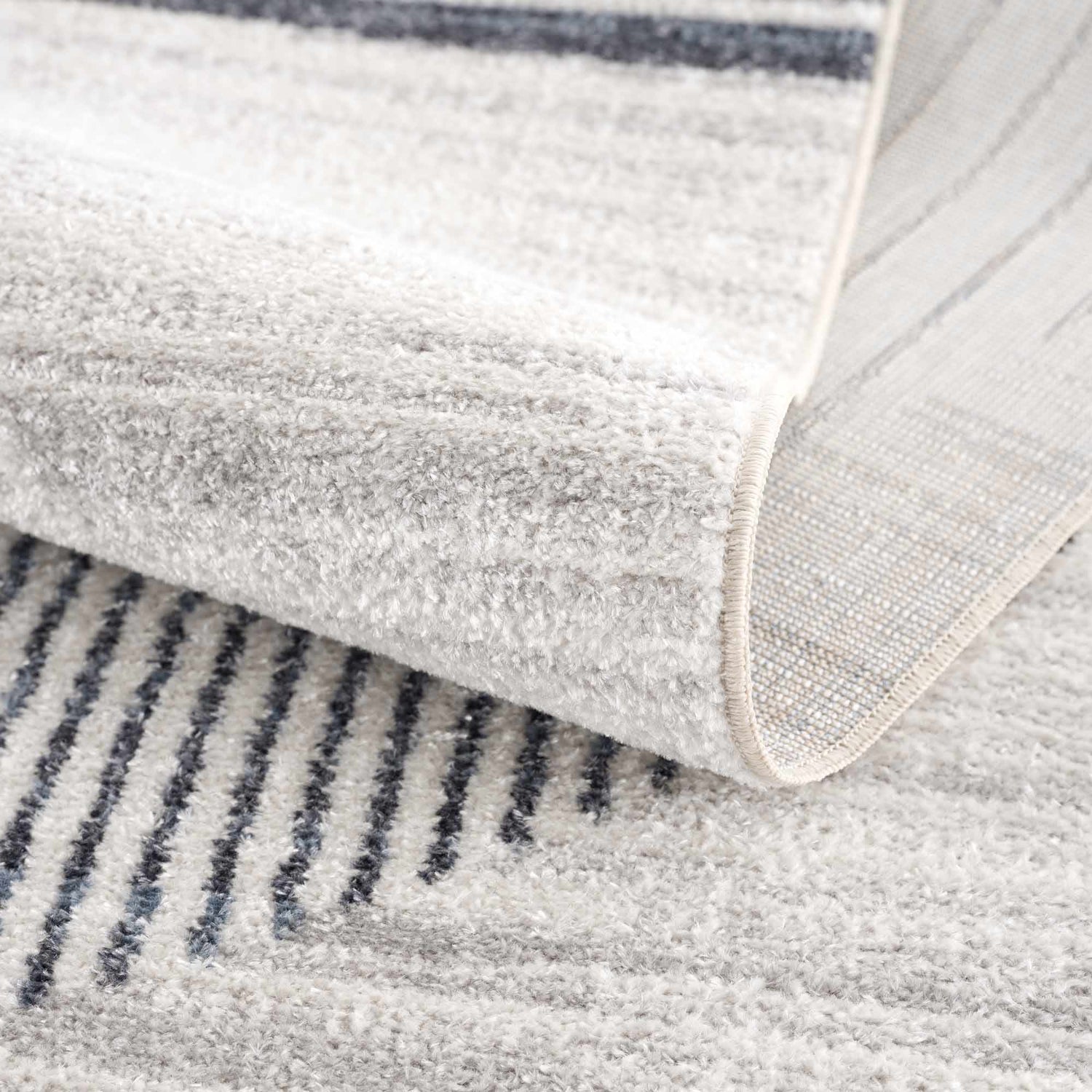Close-up of the Thad Medium Gray Washable Area Rug showing its geometric stripe pattern and soft, textured pile. Fold