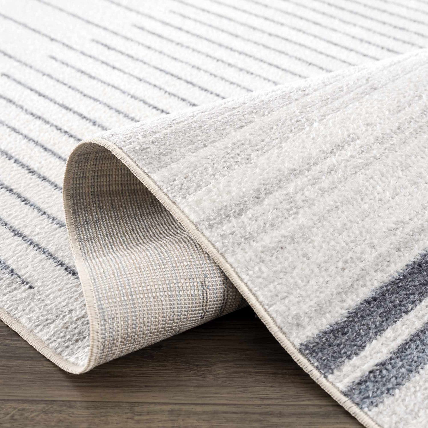 Close-up of the Thad Medium Gray Washable Area Rug, showing its bone and gray linear geometric pattern and soft, textured pile. Fold