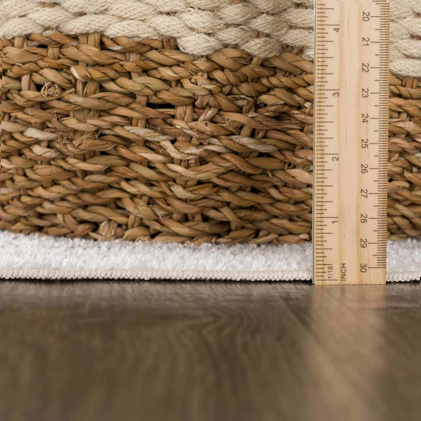 Close-up of the bone-colored, plush pile and braided edge of the Thad Medium Gray Washable Area Rug, with a ruler. Pile