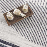 Close-up of the Thad Medium Gray Washable Area Rug with a geometric stripe pattern and decorative pineapples. Styleshot