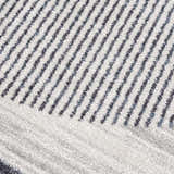 Close-up of the Thad Medium Gray Washable Area Rug, featuring a textured geometric stripe pattern in bone, gray, and dark gray. Texture