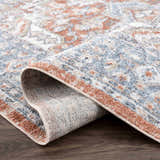 Close-up of Ember Washable Area Rug in Beachhouse. Traditional style rug with blue, white, and copper floral pattern. Fold