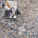 Close-up of the Aurum Blue & Beige Washable Area Rug showing its traditional pattern and soft texture. Books and glasses on top. Styleshot