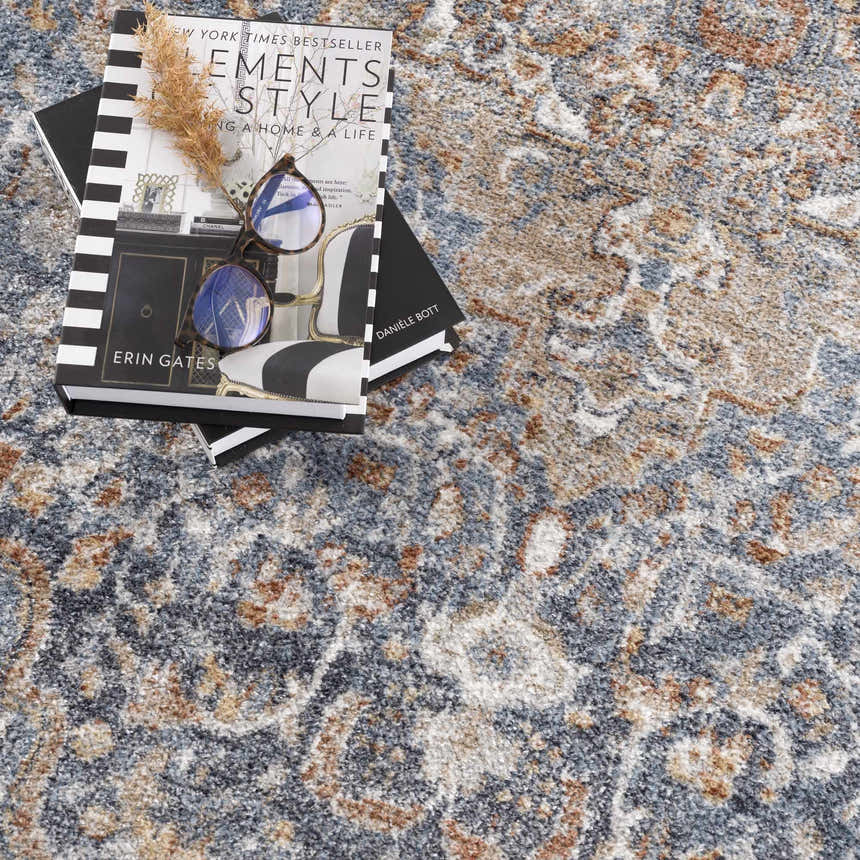 Close-up of the Aurum Blue & Beige Washable Area Rug showing its traditional pattern and soft texture. Books and glasses on top. Styleshot