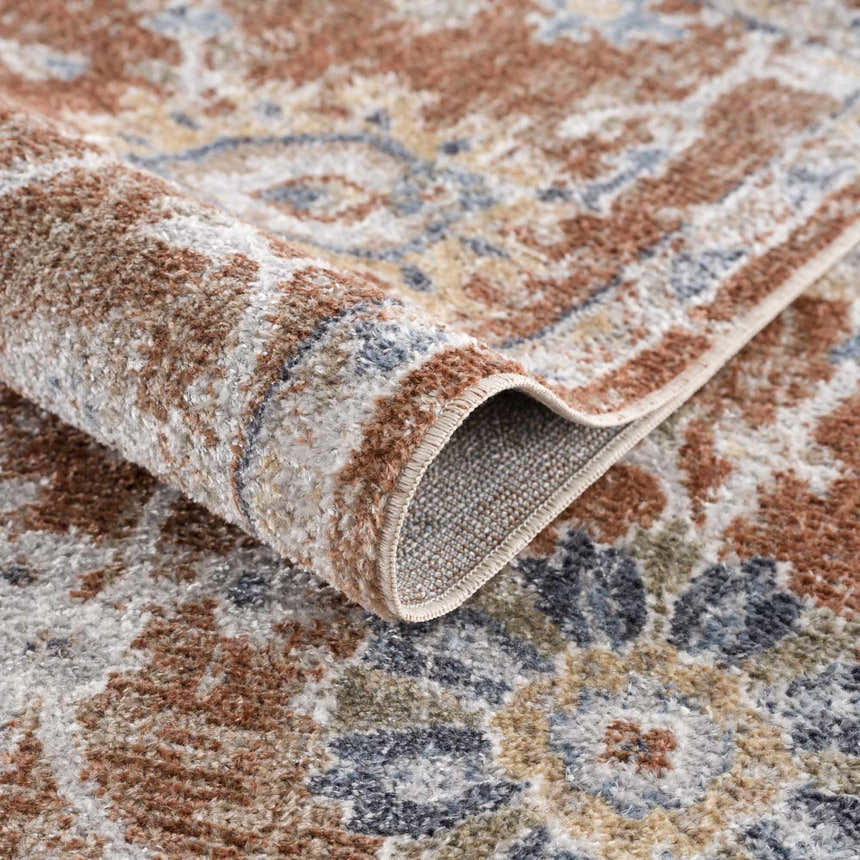 Close-up of the Chavi Washable Area Rug, showcasing its traditional floral pattern and soft charcoal, clay, and brown colors. Fold