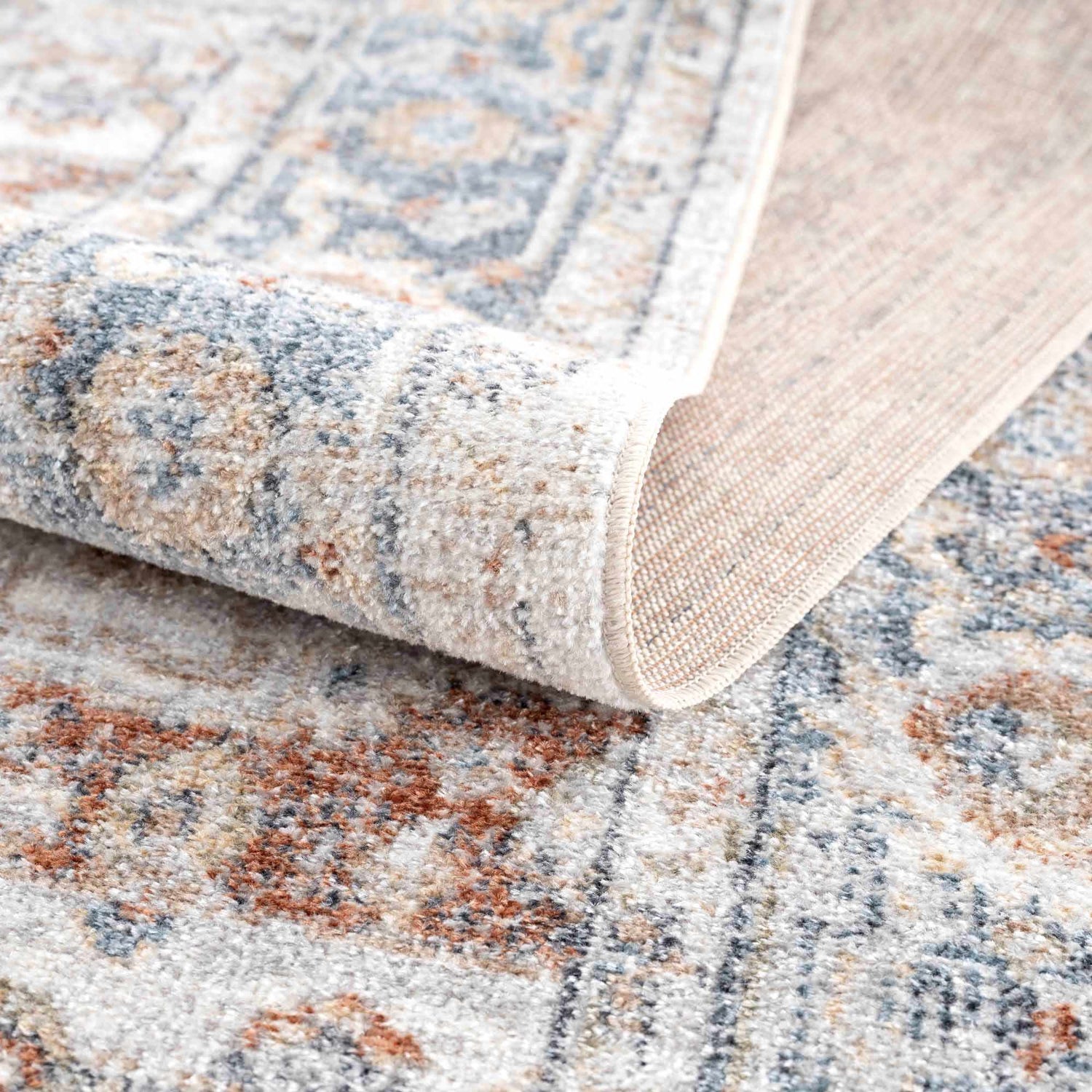 Close up of the Neta Red & Blue Washable Rug showing its flat pile, oriental pattern, and colors like driftwood and nutmeg. Fold