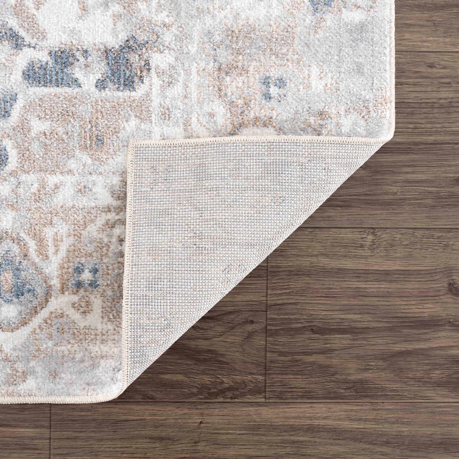 Close-up of a Dobry Boutique Washable Rug showing its blue, tan, and off-white vintage pattern and woven backing. Fold