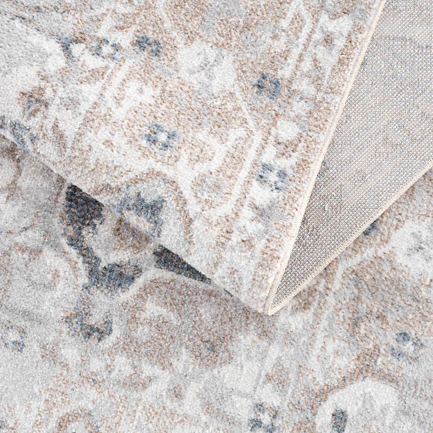 Close up of Dobry Boutique Washable Rug. Blue, off white, and tan vintage oriental pattern. Machine woven polyester rug. Fold