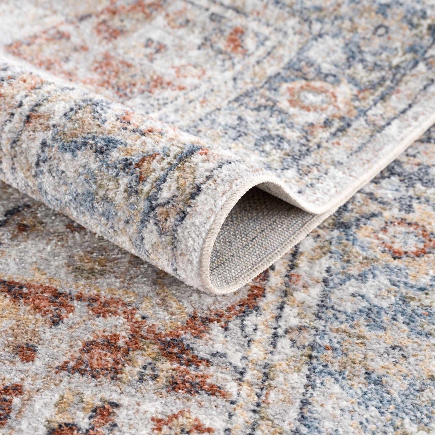 Close-up of the Akram Gray & Orange Washable Area Rug, showing the traditional vintage pattern and soft polyester texture. Fold