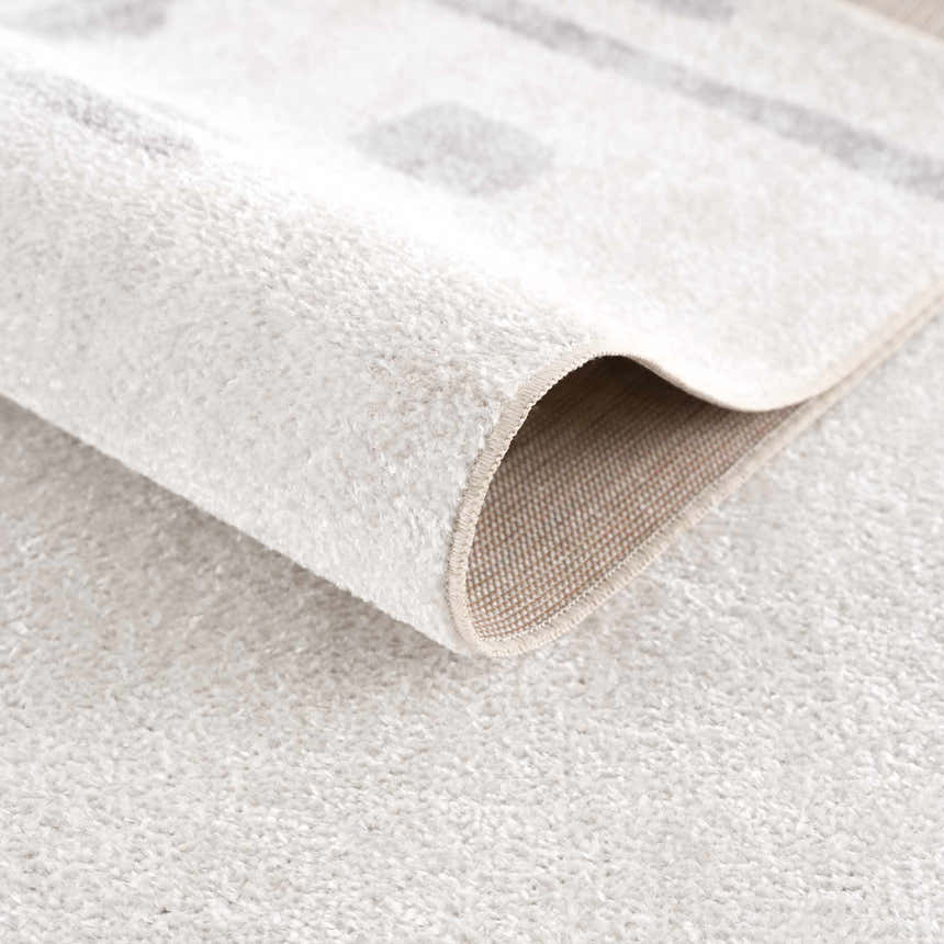 Close-up of the Eitan Modern Washable Off-White Rug, showing its soft, plush texture and abstract light gray pattern. Fold