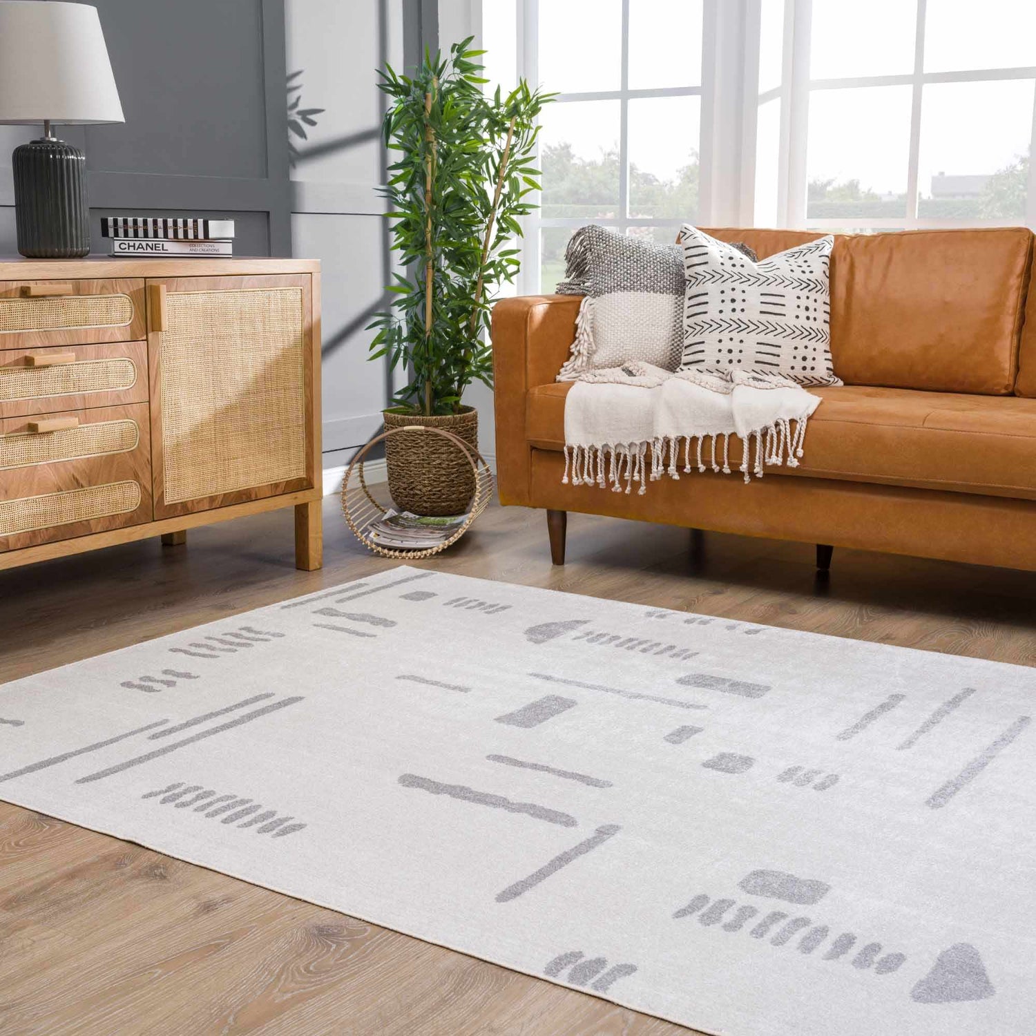 Living room scene with a modern Eitan Off-White Rug, tan leather sofa, wood cabinet, and large windows. Roomscene-Rectangle