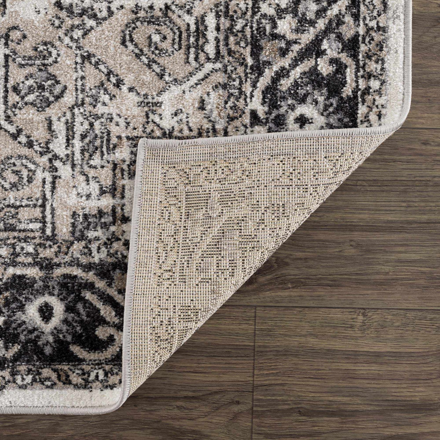 Close-up of the Cabacungan Washable Area Rug showing its black, gray, and beige vintage-style pattern and woven texture. Fold