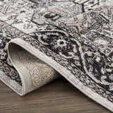 Close-up of the Cabacungan Washable Area Rug. Bohemian vintage design in black, gray, light beige, and taupe colors. Fold