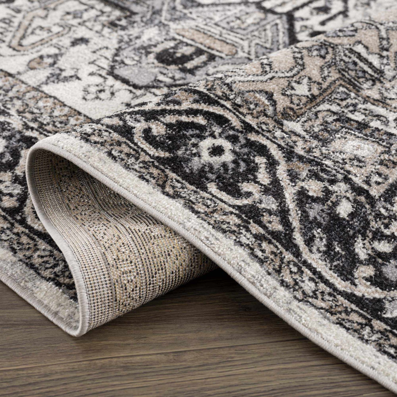 Close-up of the Cabacungan Washable Area Rug. Bohemian vintage design in black, gray, light beige, and taupe colors. Fold