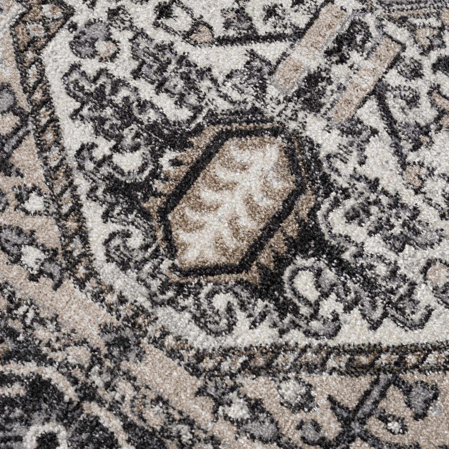 Close-up of the Cabacungan Washable Area Rug. Features a traditional pattern in black, gray, light beige, and taupe. Texture