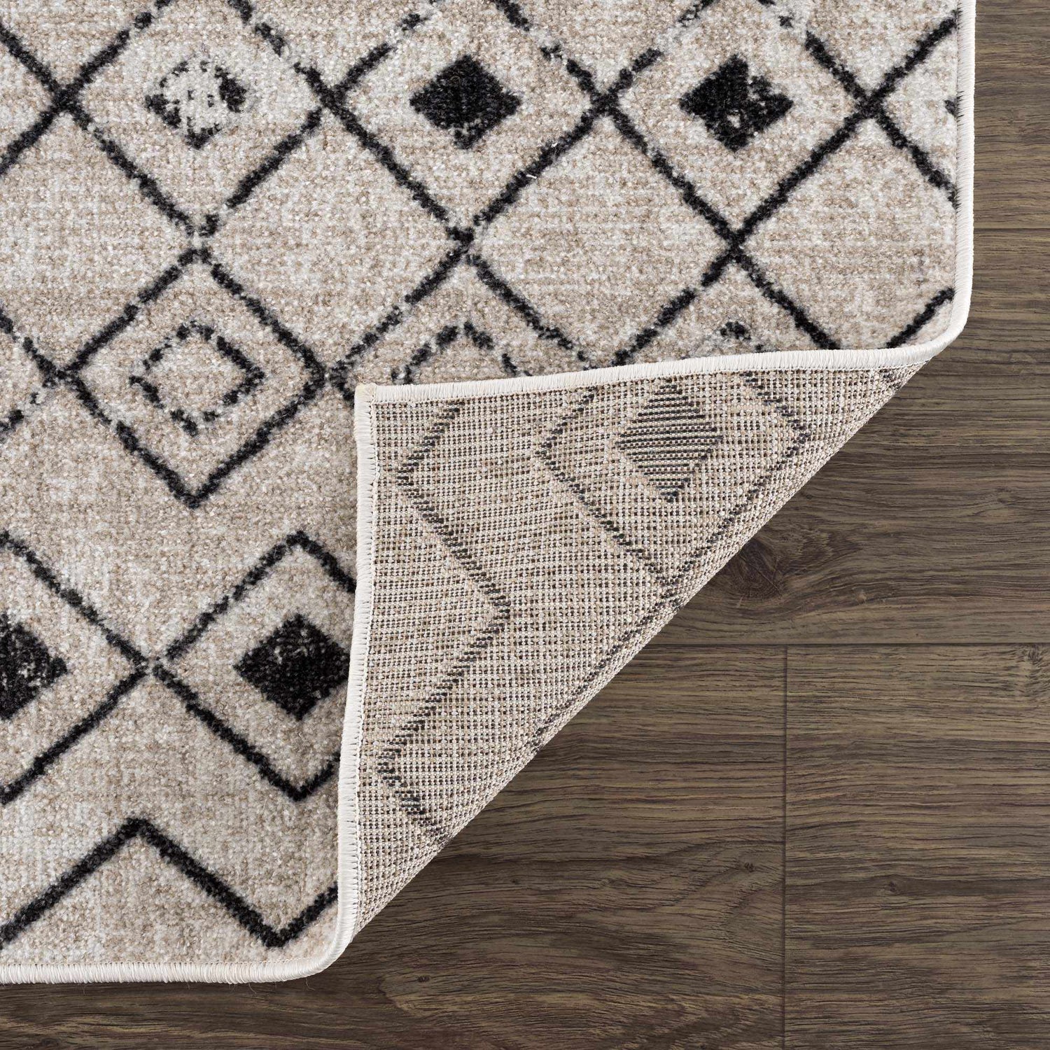 Close-up of the Joppatowne Washable Area Rug, showcasing its black geometric pattern on a cream and light beige base. Fold