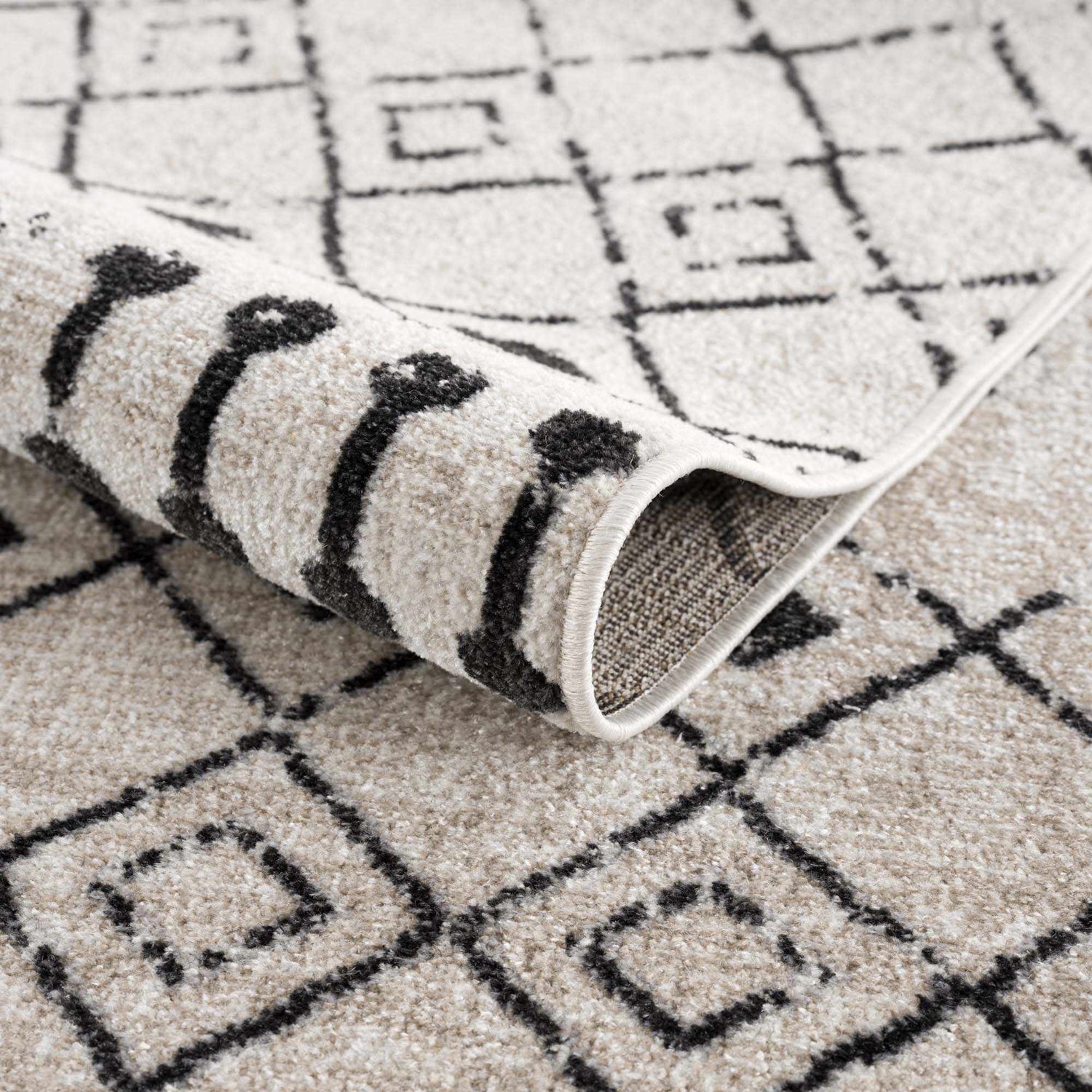 Close-up of the Joppatowne Washable Area Rug, showcasing its geometric black pattern on a cream and light beige textured surface. Fold