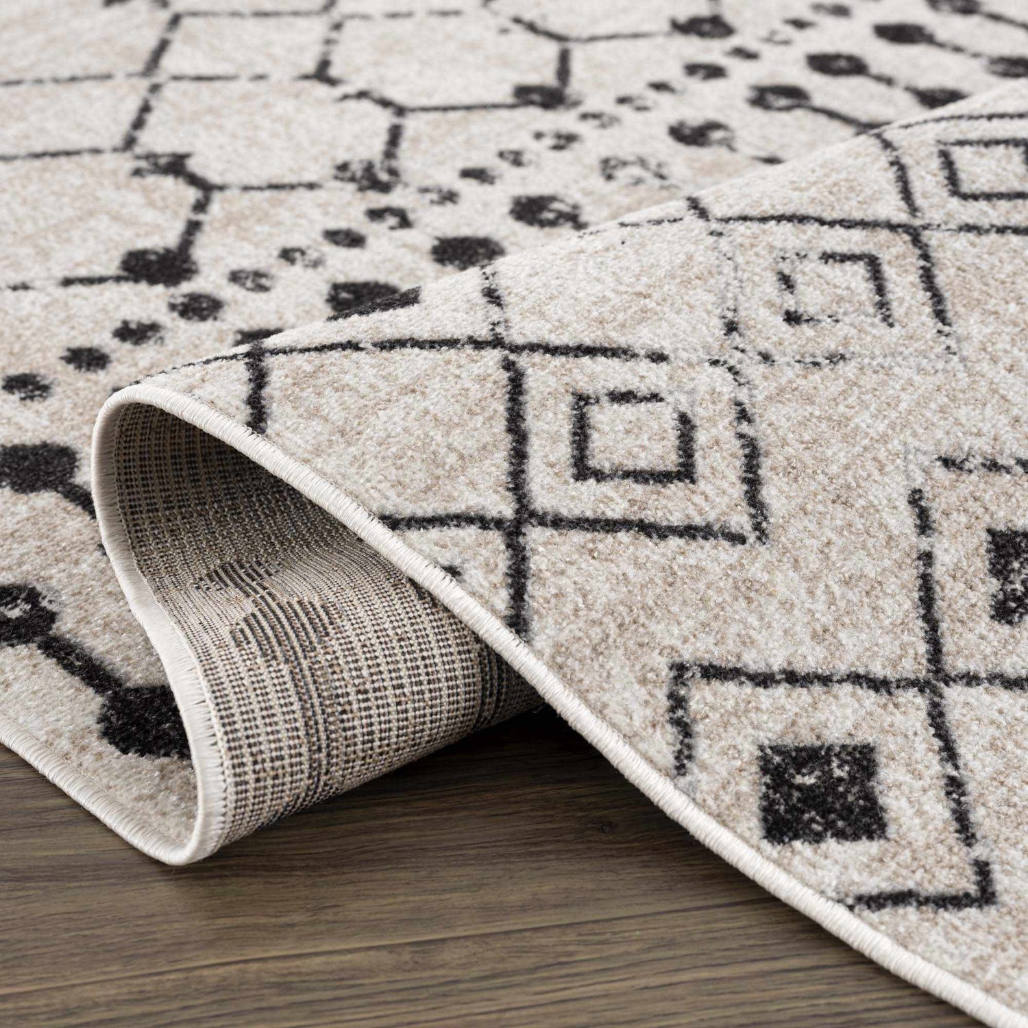 Close-up of the Joppatowne Washable Area Rug showing the geometric black pattern on cream and beige polyester. Fold