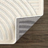 Close-up of the Deron White Washable 3D Rug showing its geometric pattern, off-white color, and underside. Fold
