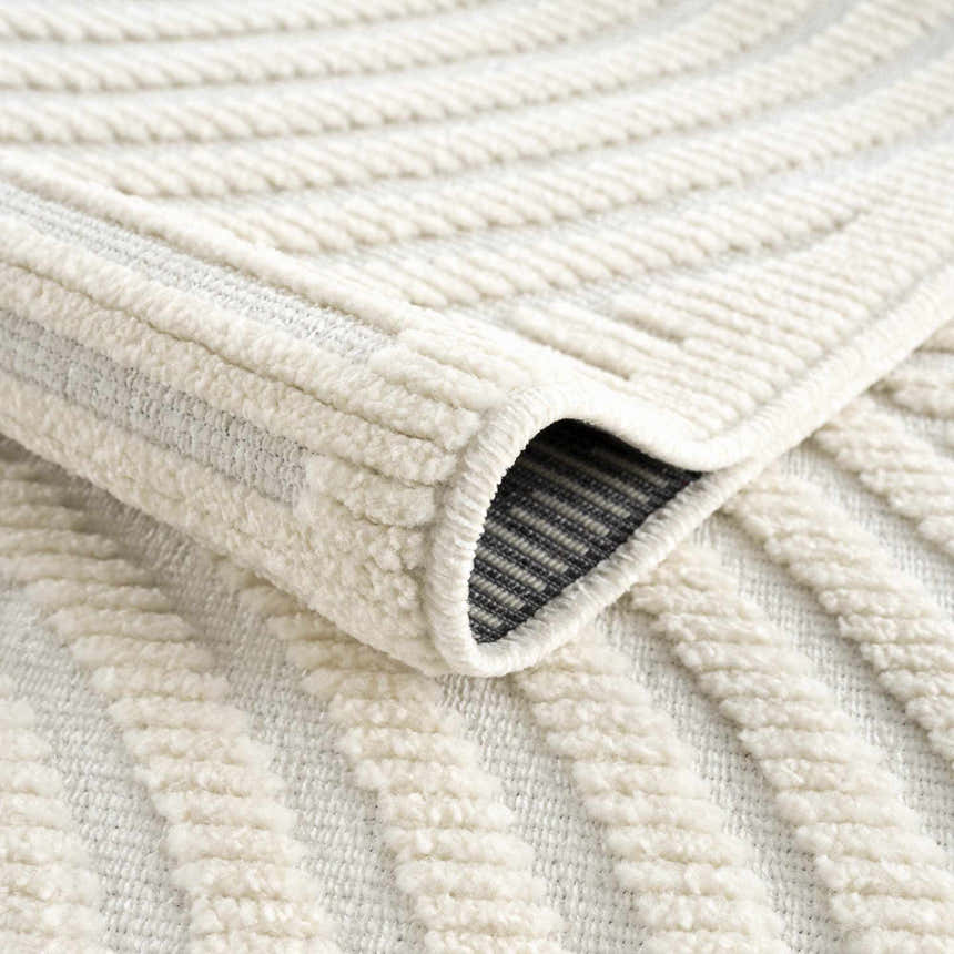 Close-up of the Deron White Washable 3D Rug showing its off-white color, geometric pattern, and textured, machine-woven construction. Fold