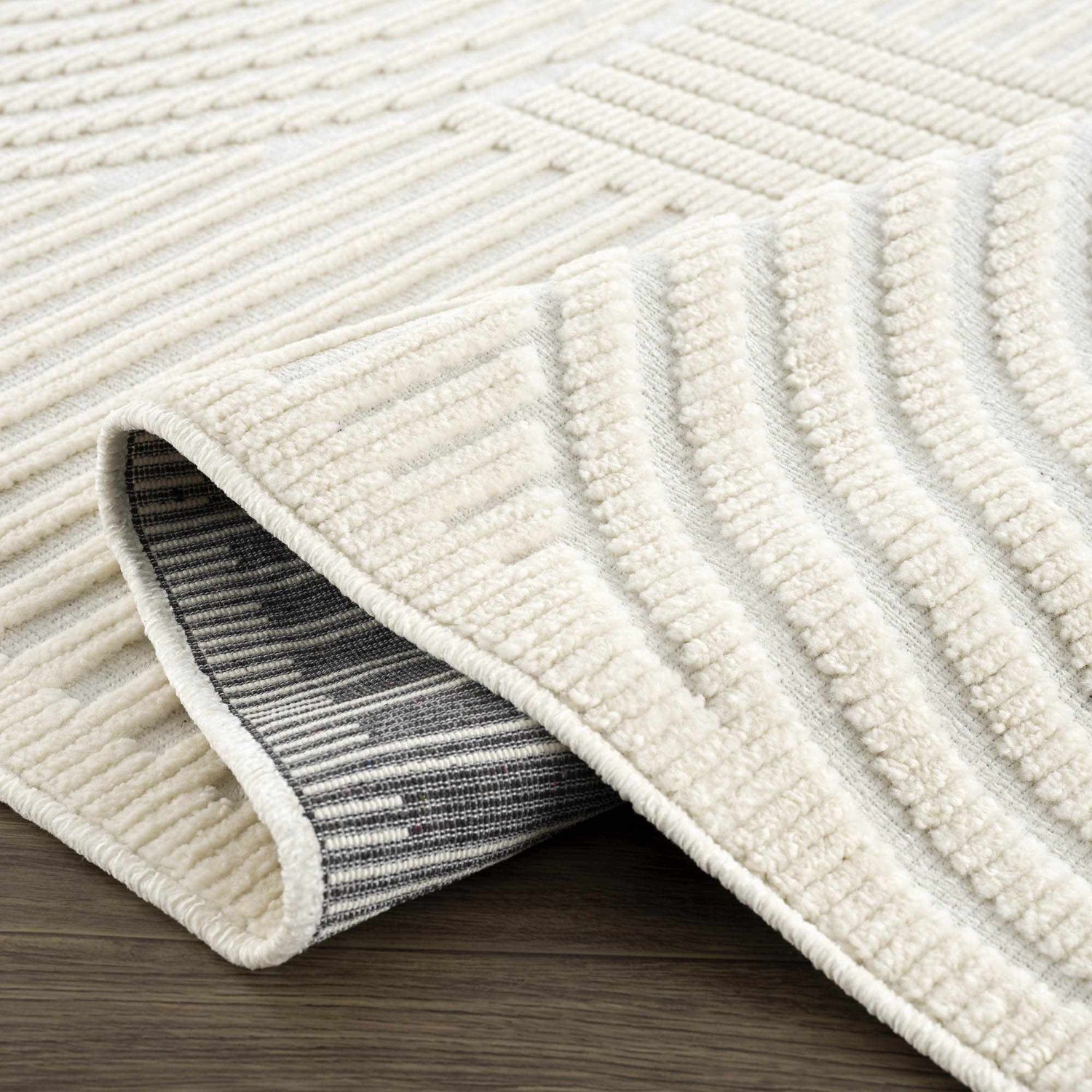 Close-up of the Deron White Washable 3D Rug showing its off-white color, geometric pattern, and textured, machine-woven construction. Fold