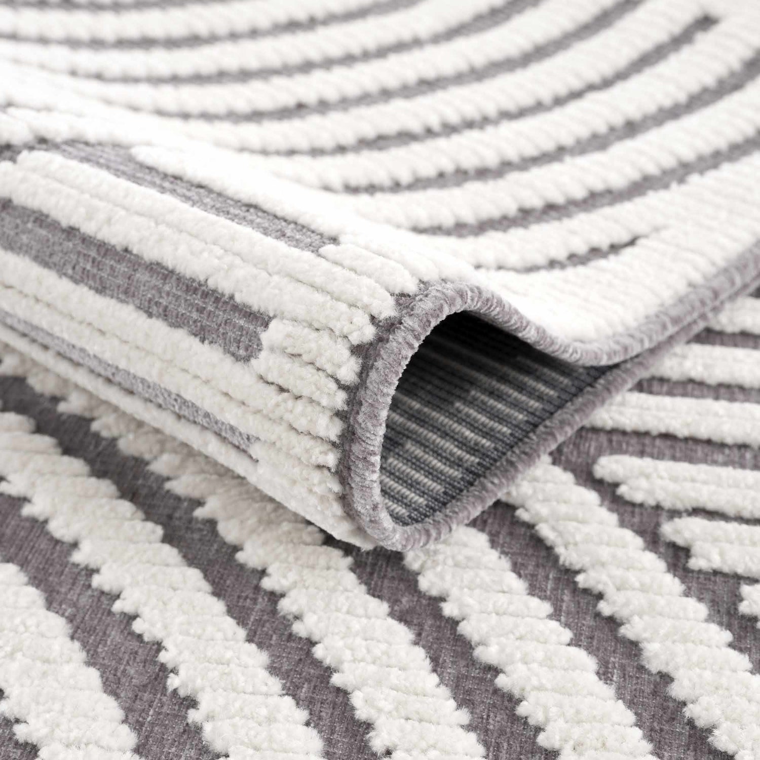 Close-up of the Deron Gray Rainbow Washable Rug showing gray and white geometric stripes and soft, textured pile. Fold