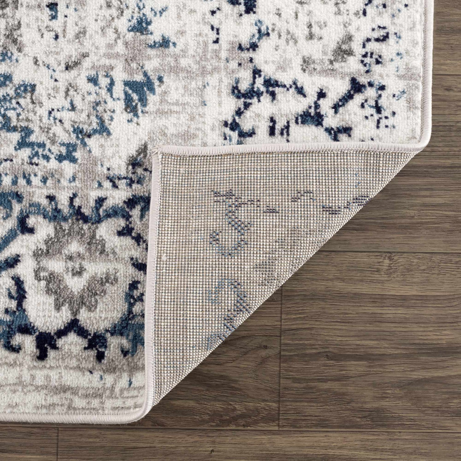 Close-up of the Duena Area Rug showing the traditional blue and light gray pattern and rug backing. Fold
