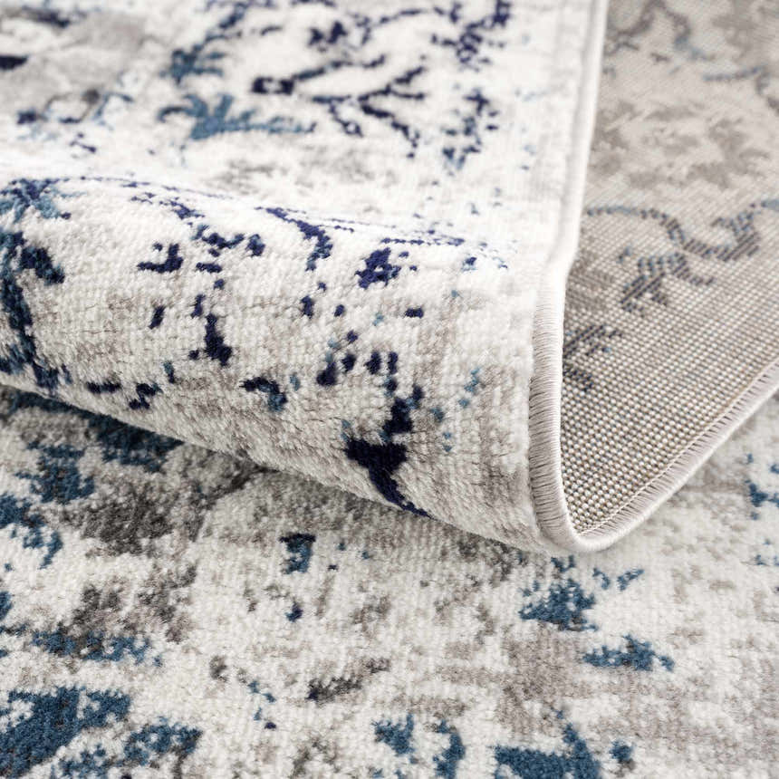 Close-up of the Duena Area Rug showing its blue and light gray traditional vintage pattern and machine woven texture. Fold