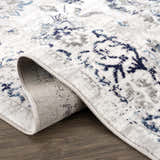 Close-up of the Duena Area Rug showing its blue and light gray traditional vintage pattern and machine-woven construction. Fold