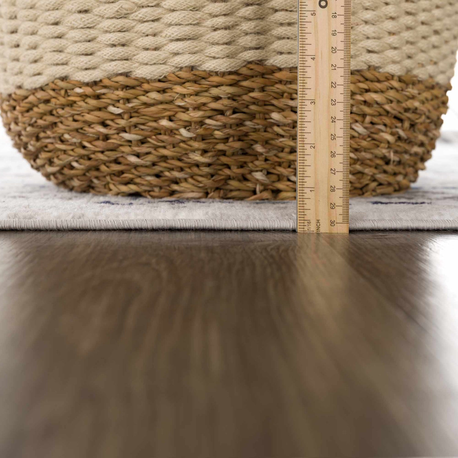 Close-up of the Duena Area Rug showing its light gray and blue traditional pattern with a ruler for scale. Pile