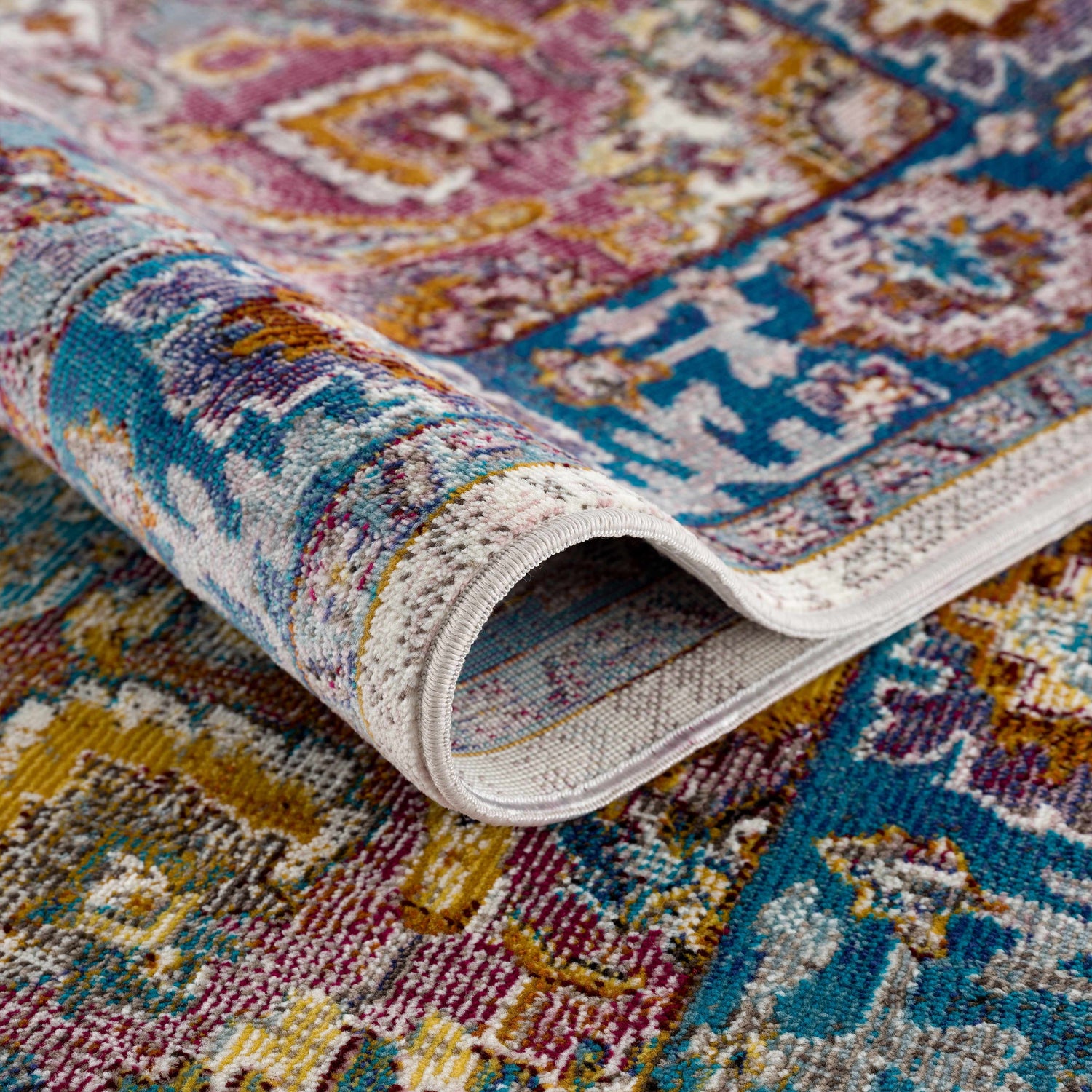 Close-up of the Mardin Colorful Area Rug, showing its blue, pink, and mustard vintage-style pattern and soft texture. Fold