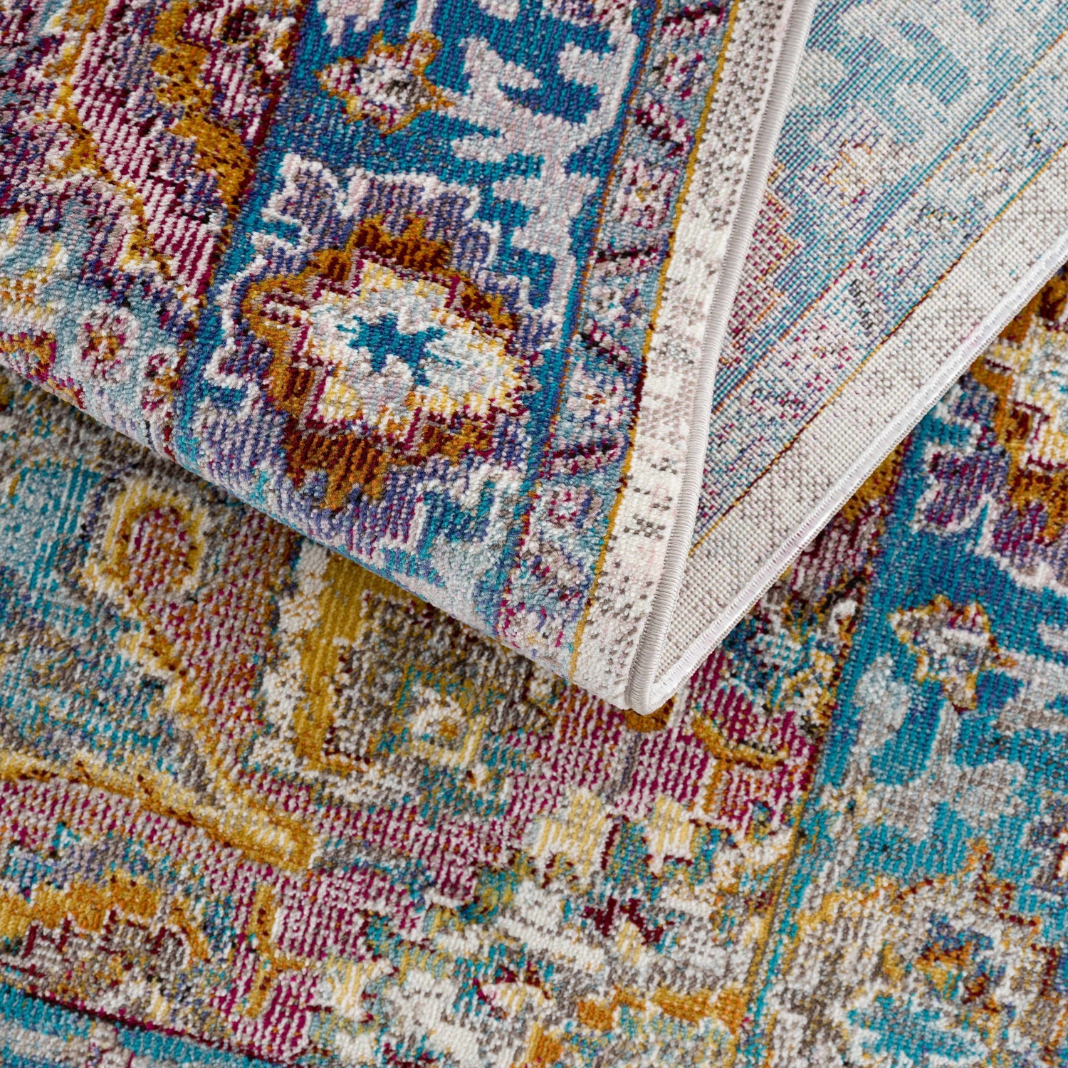 Close-up of the colorful Mardin Area Rug. Features blue, mustard, pink, and purple hues in a vintage-inspired pattern. Fold