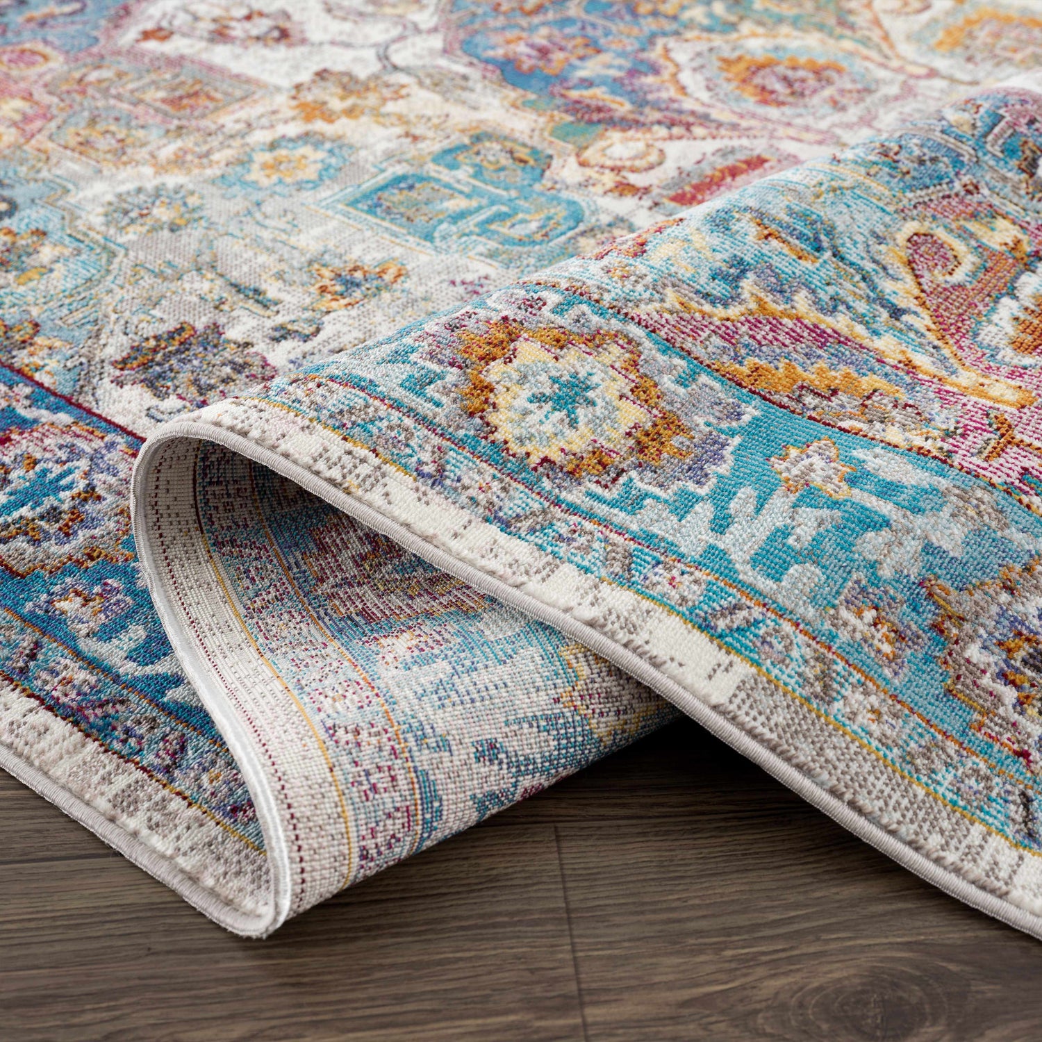 Close-up of the Mardin Colorful Area Rug showing its blue, pink, and mustard vintage-inspired pattern and soft texture. Fold