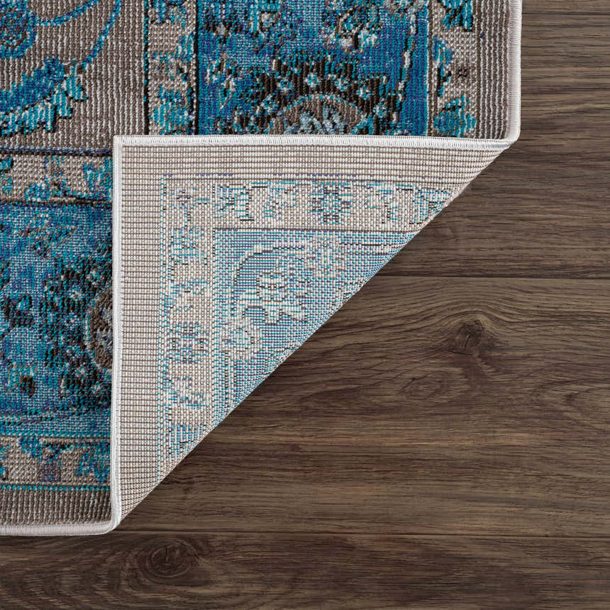 Close-up of Mardina Turquoise area rug showing beige and turquoise vintage pattern and rug backing on wood floor. Fold