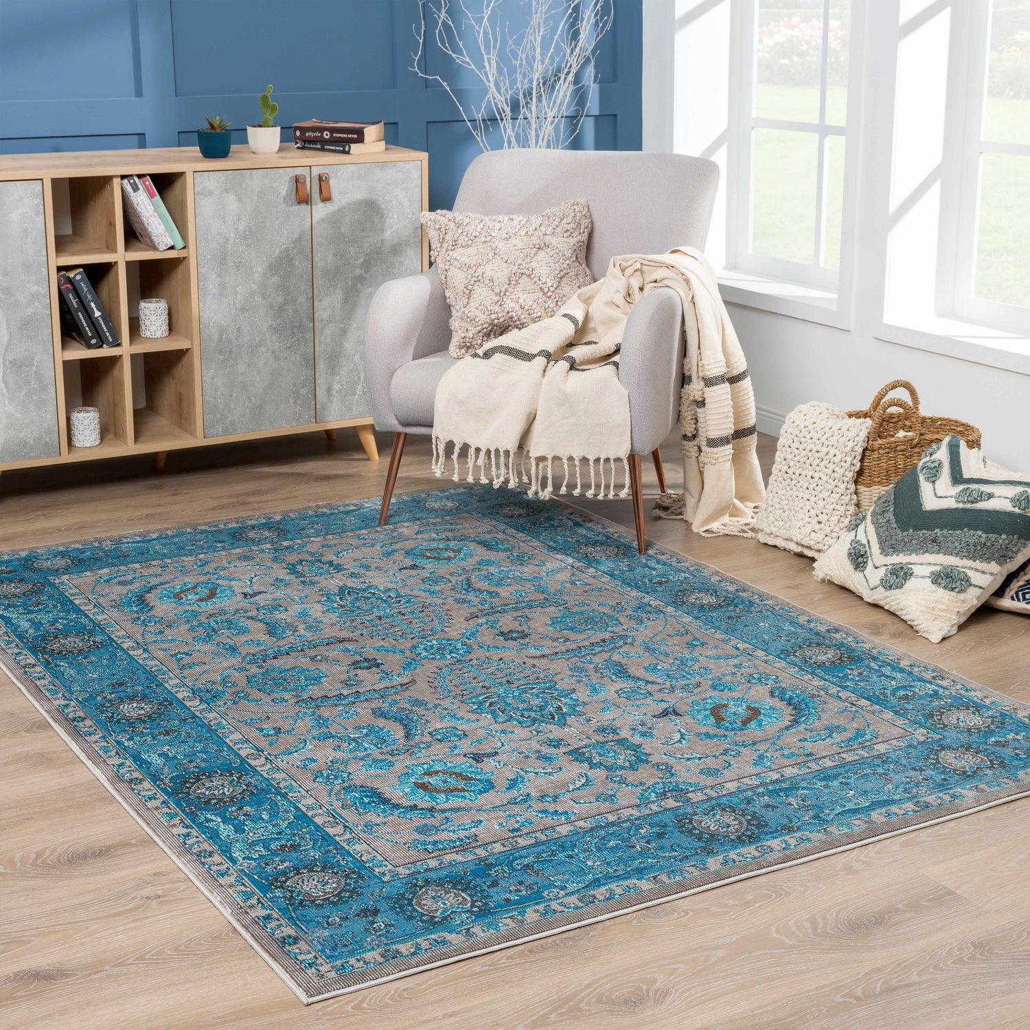 Living room scene with Mardina Turquoise Area Rug, beige armchair, wood cabinet, and natural light. Roomscene-Rectangle