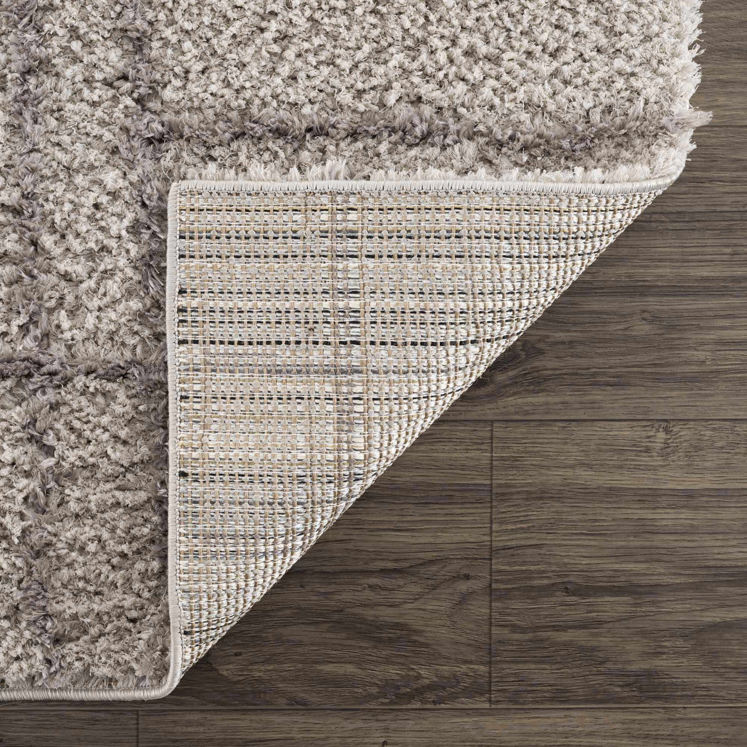 Close-up of the Andia Gray Area Rug showing its silver shag texture and woven backing on a dark wood floor. Fold