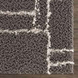Close up of the Andia Charcoal Area Rug showing the gray shag texture and white geometric pattern. Swatch